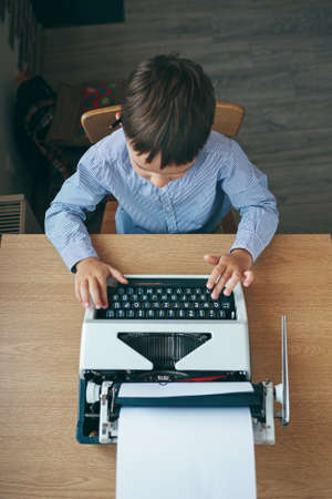 Top view, preschool journalist boy sitting at table and typing typewriter with  a pencil on the top of year. Businessman using typewriter at desk in office. Business and new technology.の写真素材