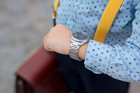 Silver watch on the hand of future businessman in blue shirt, with brifcase and yellow suspenders....