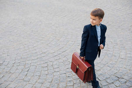Concept future businessman. High angle of businessman in formal wear standing on pedestrian street carrying a braun briefcase looking to right, urban gray pavage stone background. Copy space.の写真素材