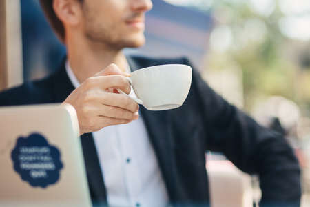 Close-up hand of young businessman with handsome masculine chin in formal wear holding cup, mug of coffeeの写真素材