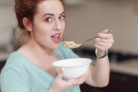 Beautiful pregnant woman eating with lust cereals on breakfast, enjoying meal. Yummy food for...