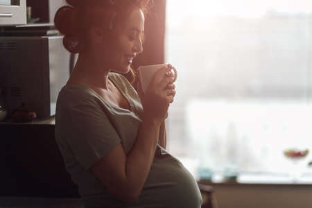 Pregnant woman emotions concept. Living feelings while drinking a cup of tea near the window with city reflection in it. Female silhouette profile picture.の写真素材