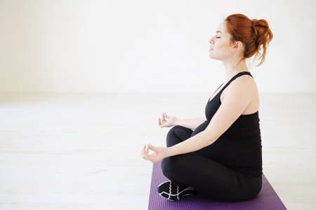 Side view pregnant woman standing in lotus pose resting hands on knees, sitting with closed eyes on...