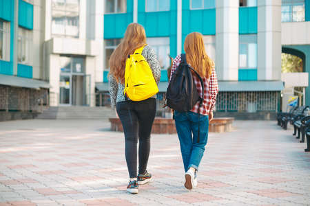 Back view of walking students with backpacks. Young college girl friends, with natural reddish hair, going to campus.の写真素材