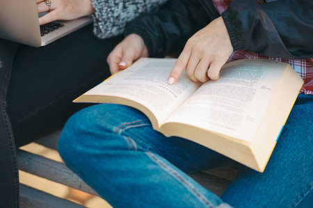 Close up on hand pointing with finger in a book while sitting on a bench outdoors -  Students preparing for university classes.の写真素材