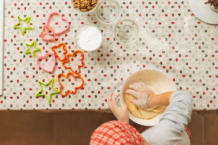Cheerful boy making dough for biscuits. Child making cookies using baking molds for Christmas...