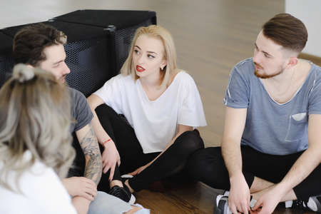 Group of young people talking while sitting on a wooden floor with music boxes in background....