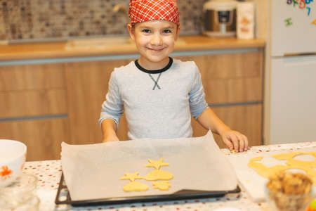 Close up cookies on backing tray ready for cook. Cute chef boy placing Christmas cookies on baking sheet. Kid hand aranging raw biscuits.の写真素材