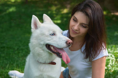 Portrait smiling woman and playful dog with tongue out, posing while sitting on the grass, outdoors