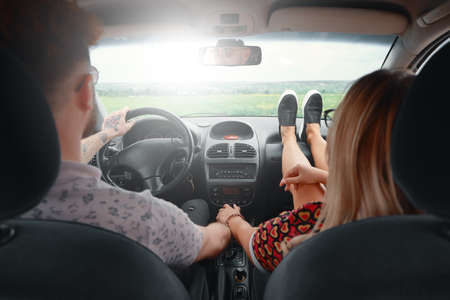 Young in love couple traveling by car to their happiness, holding their hands and looking at each other while smiling. Freedom, love and togetherness concept.の写真素材