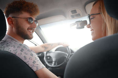 Smiling couple enjoying on a long drive in a car. Friends driving on road trip on summer day....