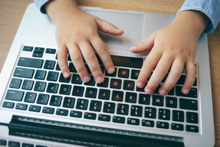 Side view, preschool boy holding his hands on the keyboard of his laptop, E-Learning concept....