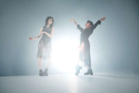 Stylish girls having fun, posing, dancing with the light play and fume. Studio shot of two gorgeous ladies moving in smother with illumination from behind, creating illusions and fantasies.の写真素材