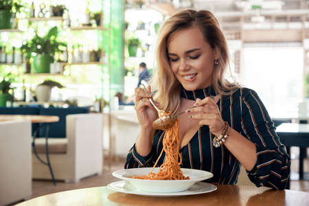 Sensual woman rolling spaghetti and keeping on a fork to eat. Beautiful girl blonde hair and...