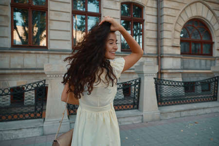 Portrait of stylish smiling, happy brunette woman walking on a street with curly hair, attractive, sunny, summer dress. Traveler, cheerful, positive, laughing young womanの写真素材