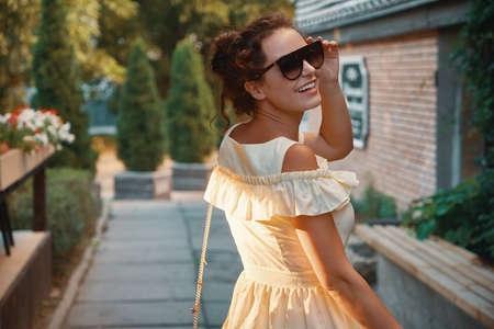 Back view portrait young city woman walking on the street, looking over shoulder, with flowers and...