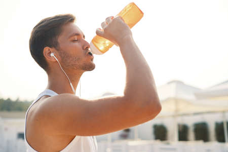 Sports Concept. Man Drinking Water After Running Workout At Beach. Portrait Of Thirsty Healthy Athletic Male With Fit Body Drinking Refreshing Drink, Resting After Running Or Training Outdoor.の写真素材