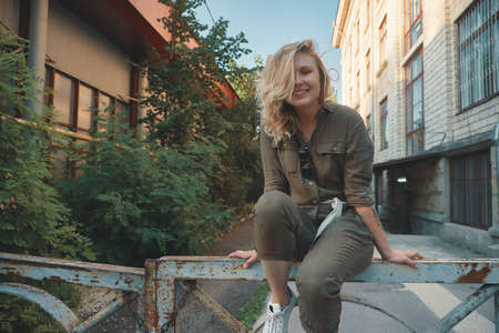 Stylish girl posing in the street sitting on a steel fence with bent legs. Urban style. Street fashion.の写真素材