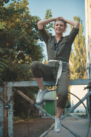 Stylish girl posing in the street sitting on a steel fence with bent legs. Urban style. Street fashion.の写真素材