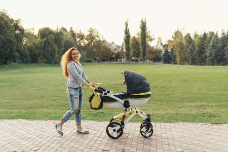 A young mother enjoying the park walk with her little child relaxing in his baby trolley.