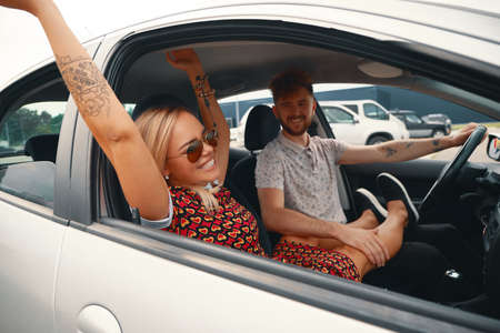Happy couple enjoying on a long drive in a car. Friends driving on road trip on summer day....