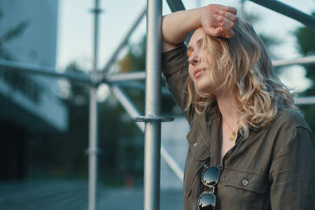 Fashion shot of carefree young woman in stylish casual romper hanging on a silver metal railing construction with a building, stairs, sky in bkgroundの写真素材