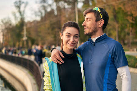 Happy sporty couple portrait. Man and woman smiling at each other while hugging. Runners outside...