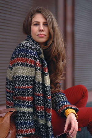 Portrait of young, beautiful woman wearing a stylish coat, red pants, orange sweater,  with a brown...