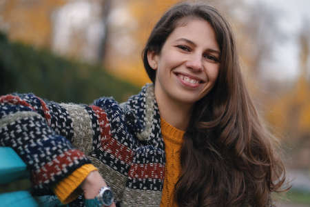 Pretty young woman in good mood posing in the autumn day, while sitting on a bench, enjoying the good weather.の写真素材