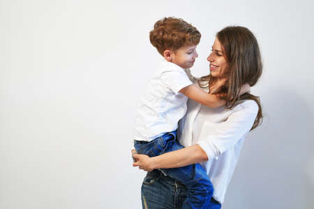 Young mother holding her preteen son smiling and looking into his eyes on white background with copy spaceの写真素材