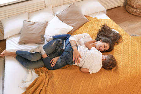 Warm and cozy scene, mom and son resting on the bed smiling and hugging. Childhood memories concept.の写真素材