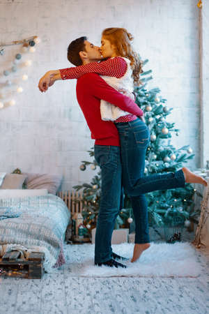 Picture showing young couple hugging and kissing over Christmas tree, full lengthの写真素材