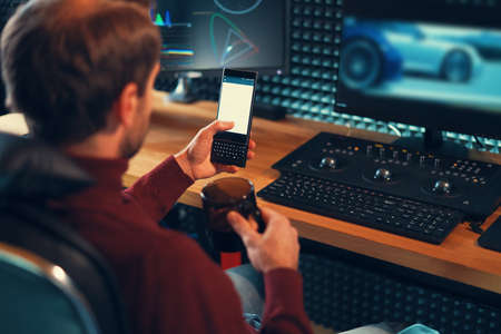 Man freelancer holding mobile phone working on footage, video, design. Cars on monitors in the background.の写真素材