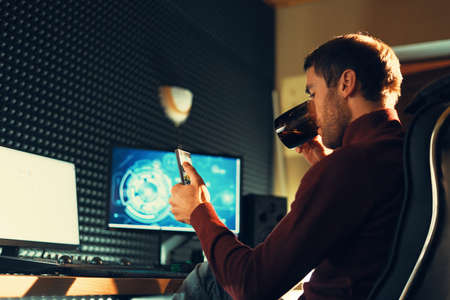 Side view man sitting in a leather chair working in the studio using a smartphone and computers....