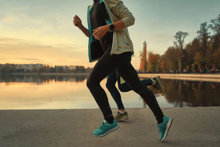 Young couple runners legs running at sunrise with lake and sky in background. Sportive people training outdoors. Down angle shot.の写真素材
