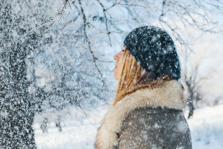 Winter portrait of young beautiful blonde woman enjoying snow flakes. Snowing winter wonderland and wishes come true concept, side view.の写真素材