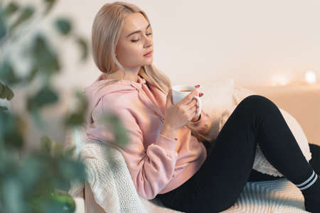 Pretty girl sitting on the sofa with a cup of coffee, tea in hands. Leisure and relax concept