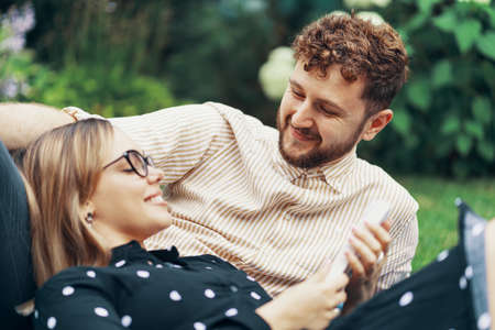 Couple in love lying on the grass in the yard of his house. Girl reading a book