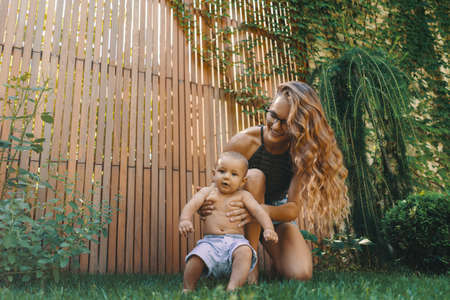 Baby boy takes his first steps with the help of mom on green grass in the backyardの写真素材