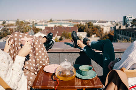 Two attractive girls enjoy a tea party on the rooftop overlooking the city. Drinking healthy buckwheat tea. Healthcare or herbal medicine concept.の写真素材