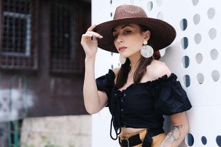 Fashionable brunette woman with long hair, wearing stylish large wicker hat, posing against a white...