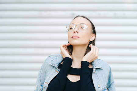 Portrait young woman with glasses. Pretty style woman with long dark hair wearing a denim jacket. Summer mood. Outdoor portrait. Background park. Street fashion photoの写真素材