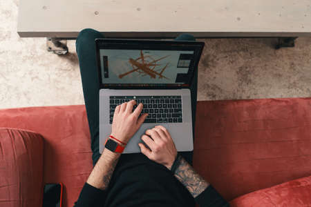 A designer working while holding a laptop on the legs sitting on a comfy couch in a modern interior....