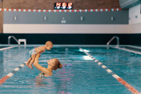 Young mother and her baby enjoying a baby swimming lesson in the pool. Child having fun in water...