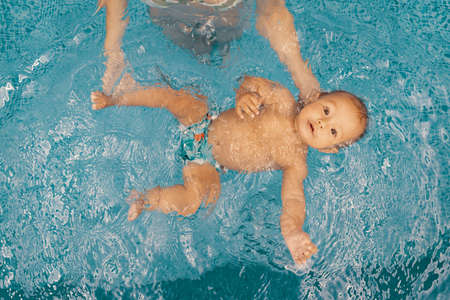 Young mother and her baby enjoying a baby swimming lesson in the pool. Child having fun in water...