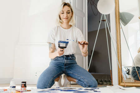 Beautiful young woman artist drawing in a comfy home interiorの写真素材