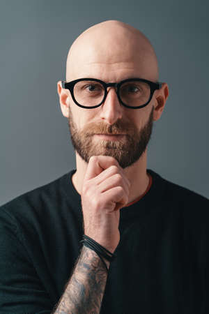 Confident stylish young bearded man wearing glasses with black frame, posing in studio o gray background.の写真素材