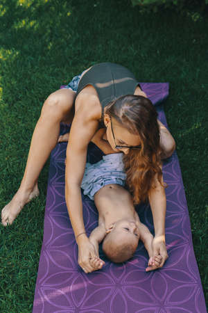 Mother doing baby yoga for her son on a mat in the backyardの写真素材
