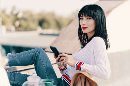 Two attractive girls enjoy a tea party. Girl with black hair is typing a message on the phone