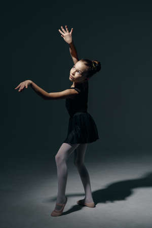 Beautiful girl ballerina dancing in light play and shadowson dark backgroundの写真素材